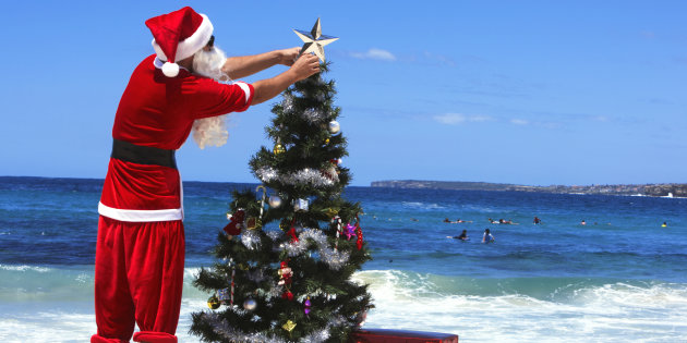 Man dressed as Santa Claus decorating christmas tree on beach, rear view